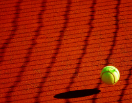 Green tennis ball bounces on red clay court